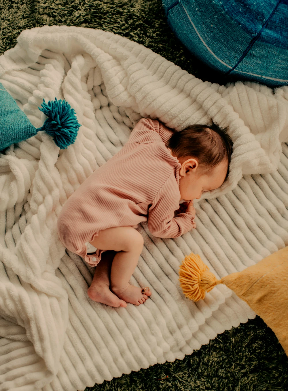 Neugeborenes Baby schläft ruhig auf weicher Decke, umgeben von bunten Kissen.